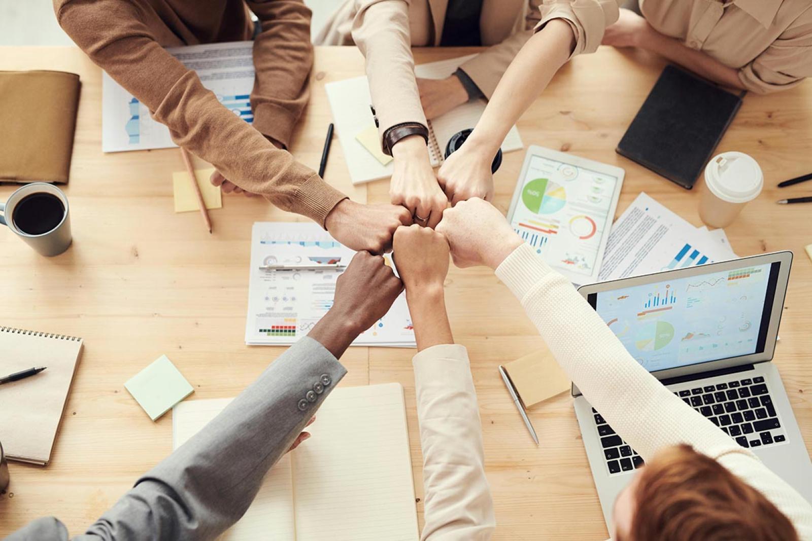Arms of six people having a fist bump over a table whilst working collaboratively 
